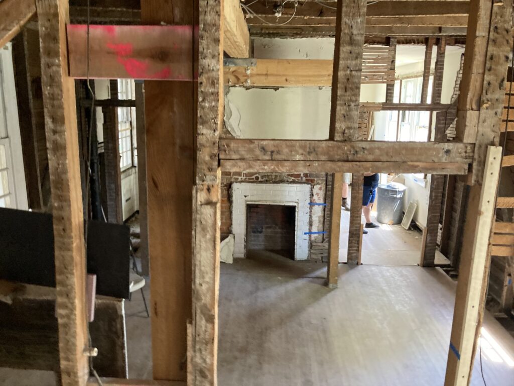 Interior of 18th-century building, revealing floorboards, fireplace, and wall boards with original nails